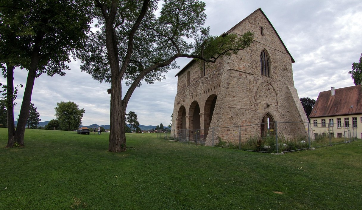 Die Ruine der Klosterkirche des Klosters Lorsch auf einer Wiese unter alten Bäumen.